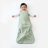 Infant wearing sage green sleep sack over white shirt lying on white surface