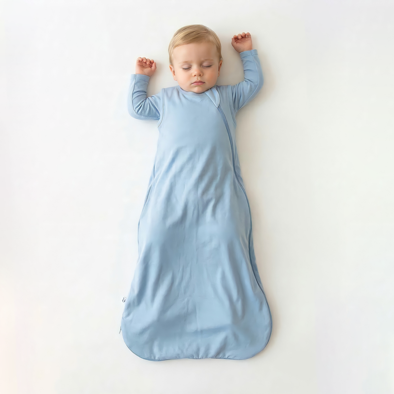 Toddler sleeping in light blue bamboo sleep sack with arms raised