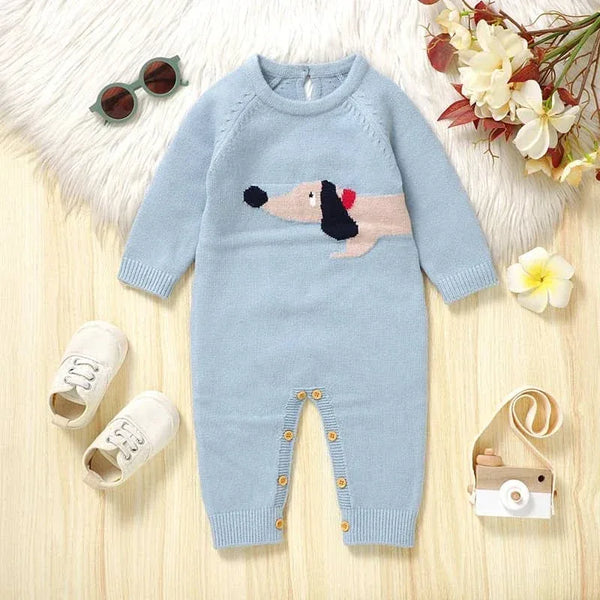 baby wearing blue dachshund baby sweater romper lying flat with white baby shoes sunglasses and toy camera nearby