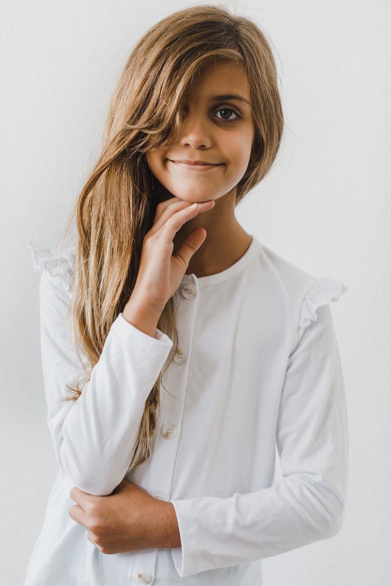 Smiling girl wearing a White Ruffle Cardigan from Mila & Rose®, showcasing playful ruffle details and a cozy fit, perfect for chilly mornings and versatile outings.