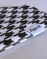 Black and white houndstooth Timeless Charm Bandana Bib with durable stitching and Baldwin Baby Co label for classic style and drool protection.