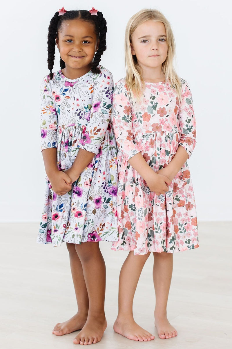 Two charming girls modeling the Midnight Rain 3/4 Sleeve Pocket Twirl Dresses, one in floral print and the other in a lovely pink floral design.