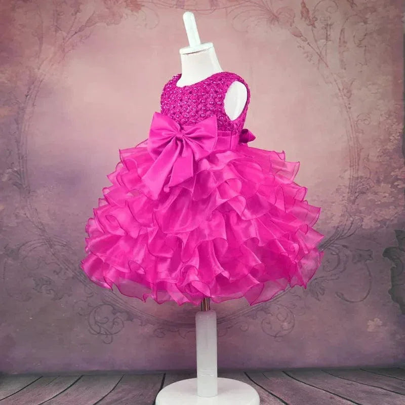 Bright pink beaded special occasion dress for girls on mannequin with large bow and ruffled skirt