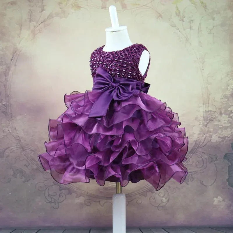 Purple beaded special occasion dress for girls displayed on mannequin with ruffled skirt and large bow
