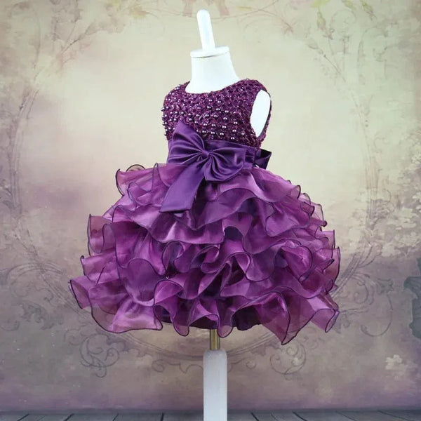 Purple beaded special occasion dress for girls displayed on mannequin with ruffled skirt and large bow