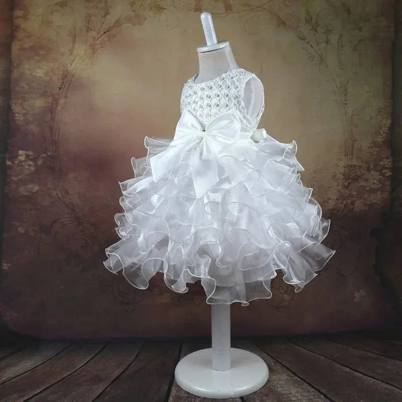 White beaded special occasion dress for girls with ruffled skirt and large bow on mannequin