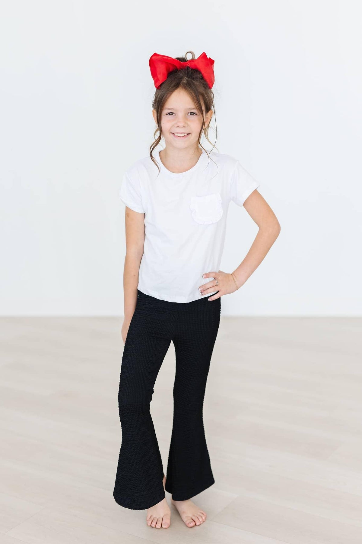 Young girl wearing black bell pants and white t-shirt with red scrunchy bell hair accessory