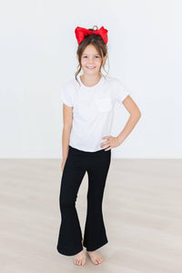 Young girl wearing black bell pants and white t-shirt with red scrunchy bell hair accessory