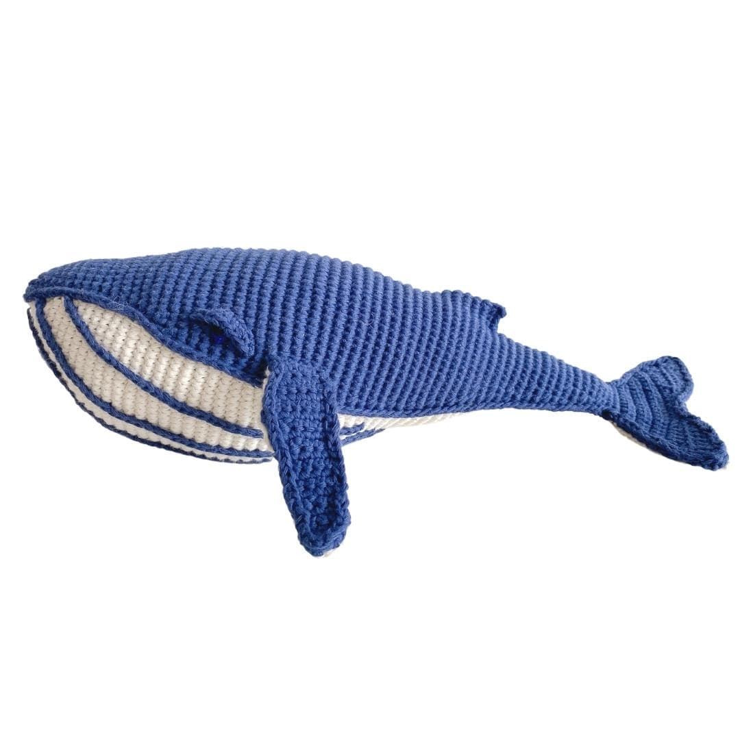 Hand-crocheted blue whale toy with pale belly and broad tail, made from soft organic cotton for imaginative play.