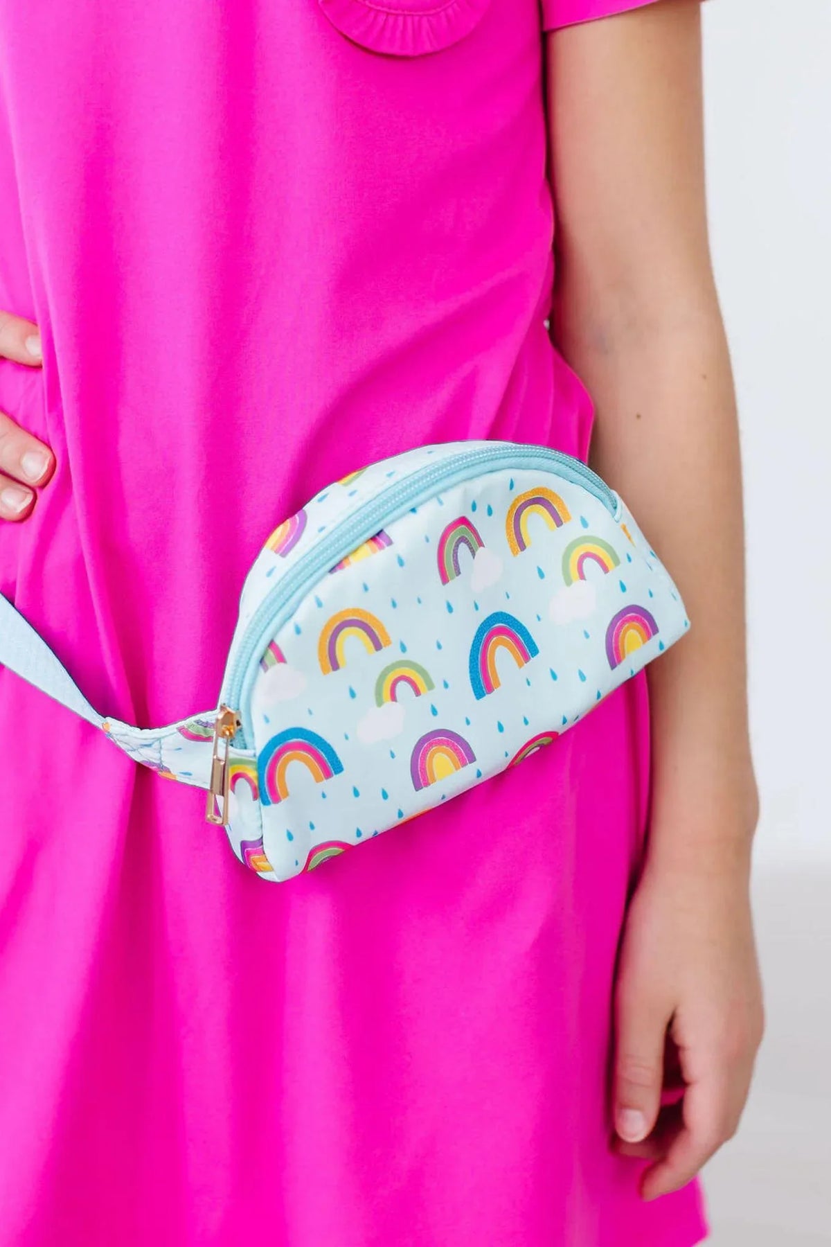 Girls pastel blue belt bag with colorful rainbow print worn over bright pink dress