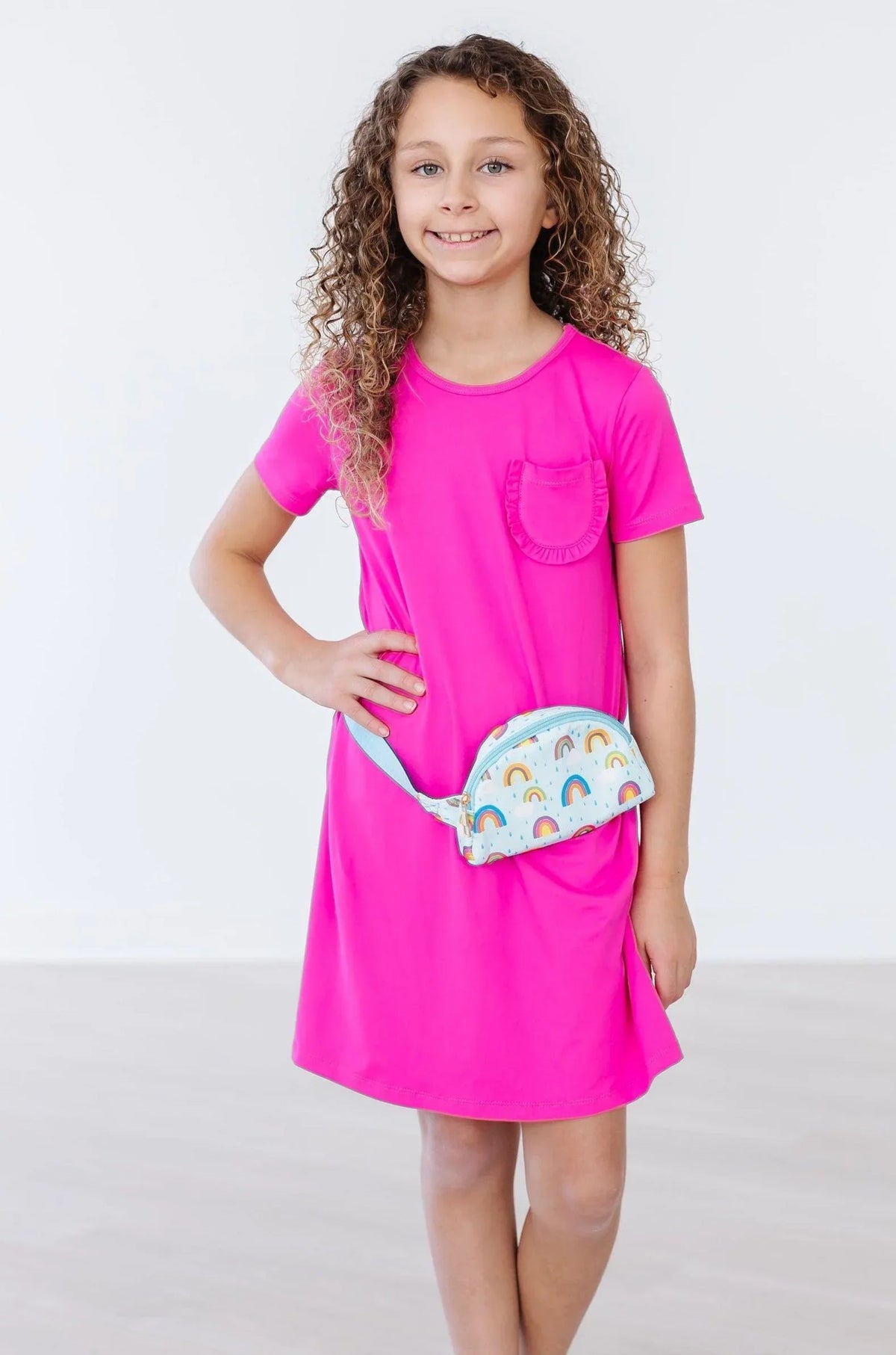 Girls light blue belt bag with rainbow print worn by girl in bright pink short sleeve dress