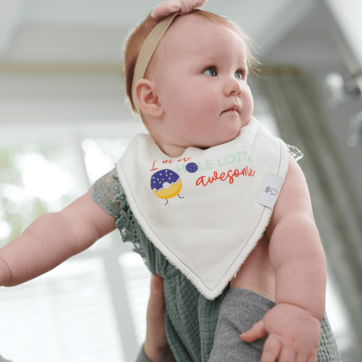 white bib muslin with colorful bird design on baby girl wearing green outfit and pink headband