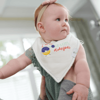 white bib muslin with colorful bird design on baby girl wearing green outfit and pink headband