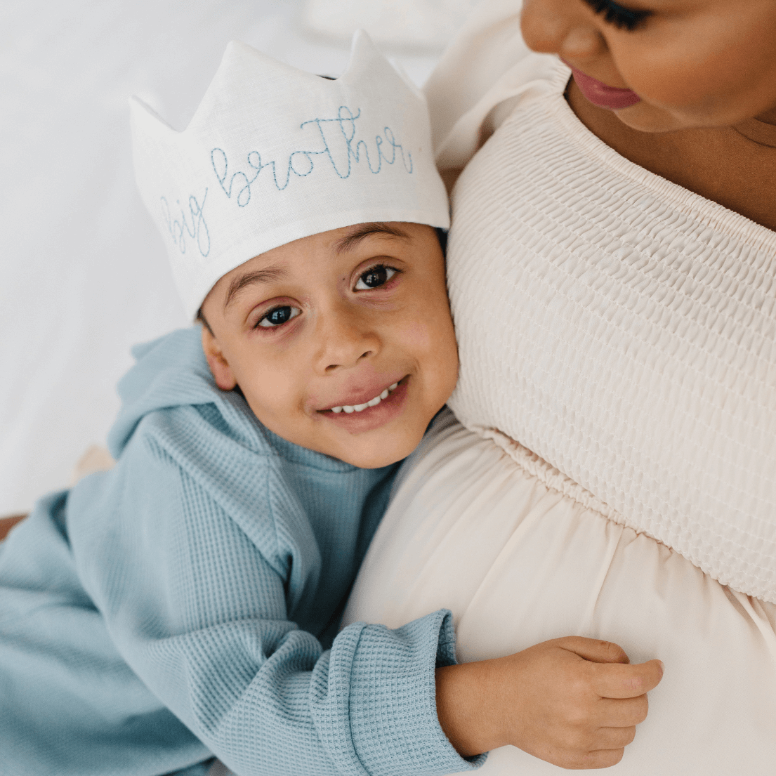 Child wearing a 'my brother' hat hugging a pregnant woman