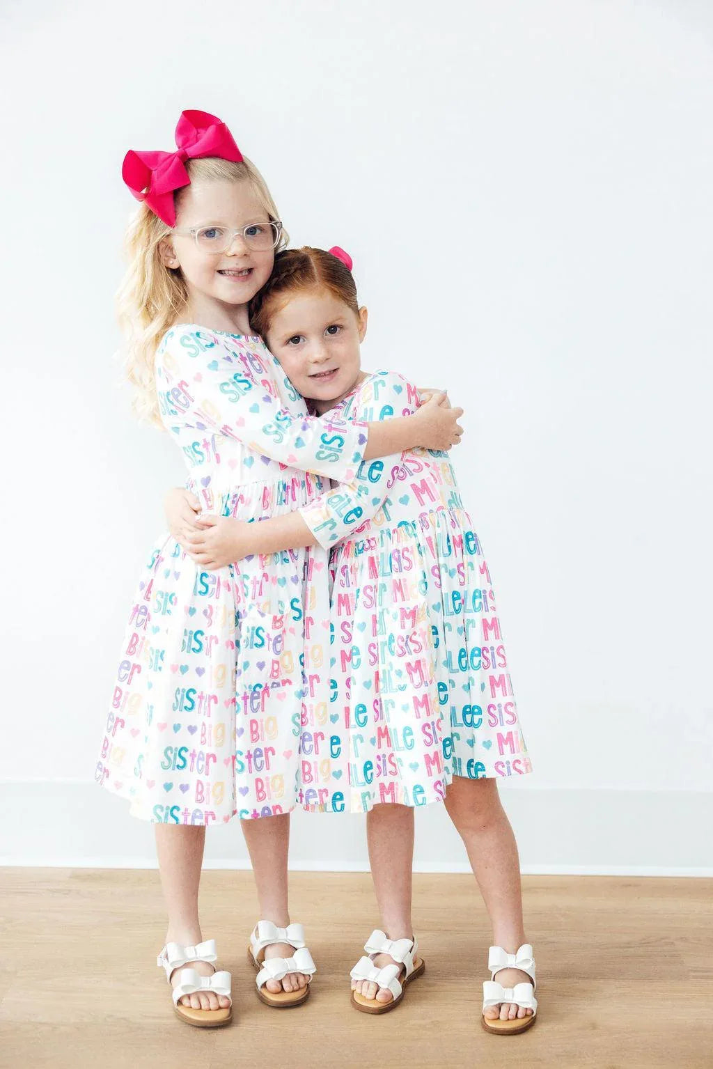 two young girls wearing colorful Mila and Rose big sister dress for girls twirl pocket dresses hugging