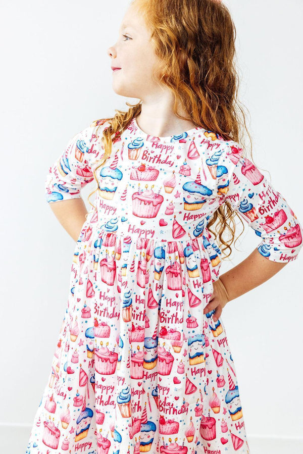 Young girl wearing colorful birthday girl dress with cupcakes and Happy Birthday print twirling