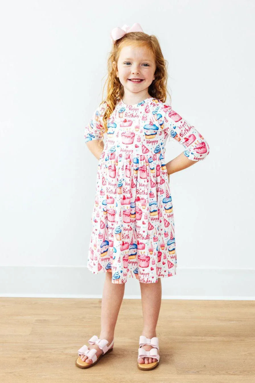 red-haired girl wearing Mila & Rose birthday girl dress with cupcakes pattern twirling and smiling