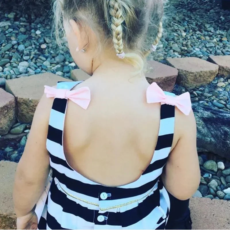 toddler girl wearing black and white striped dress for girls with pink bows standing outdoors with braided hair
