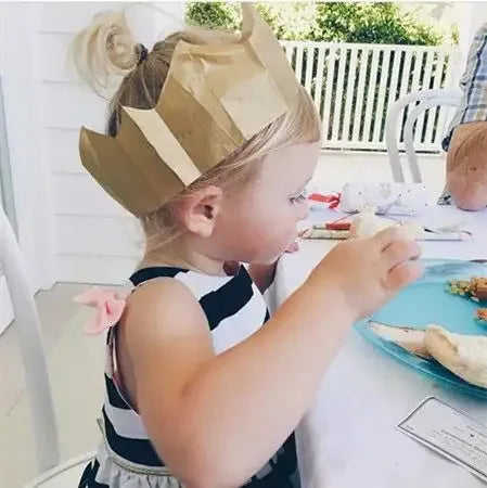 Toddler girl wearing black and white striped dress for girls and paper crown eating at a table