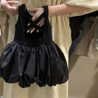 Hands holding a black girls party dress with cutouts for toddlers showing crisscross straps and puffy skirt