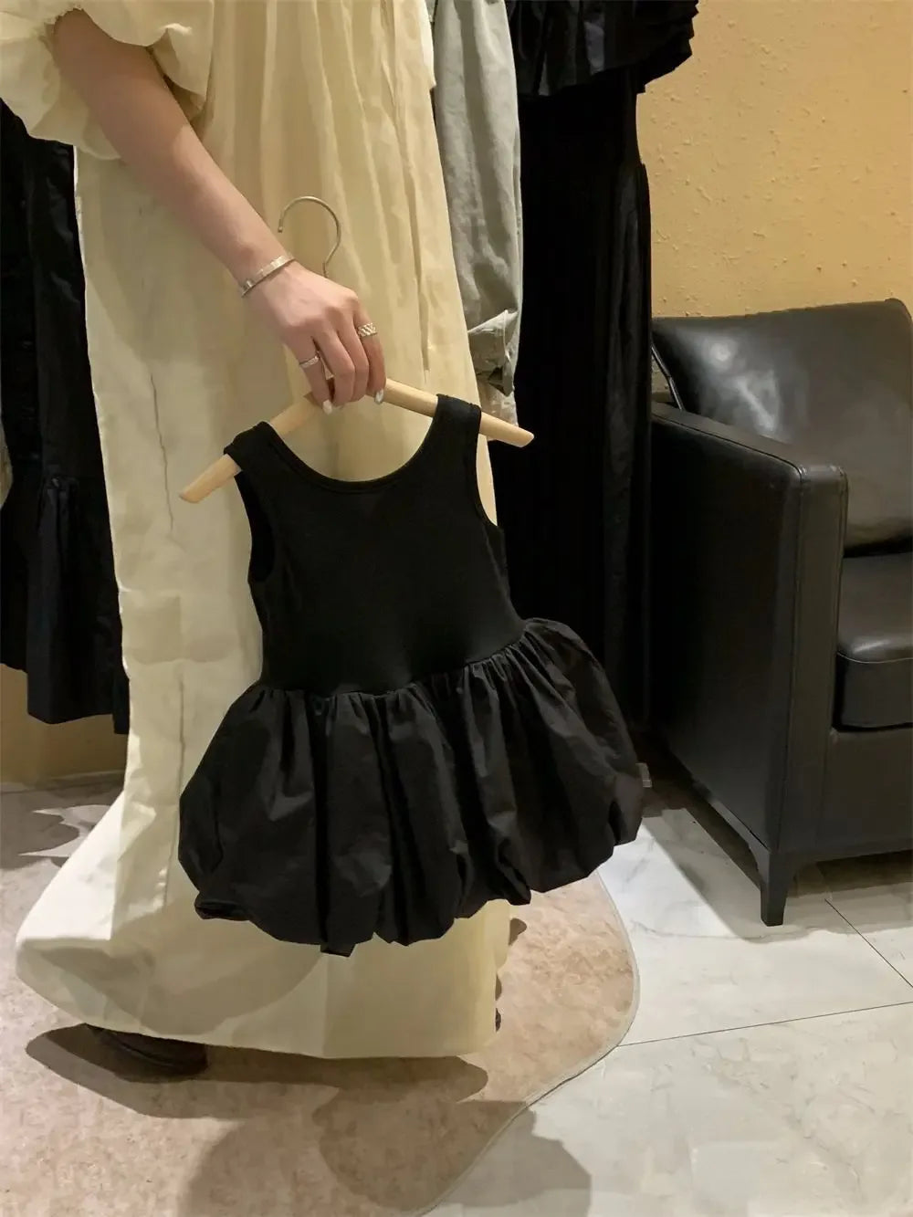 Woman holding a black girls party dress with cutouts for toddlers featuring a sleeveless design and puffy skirt