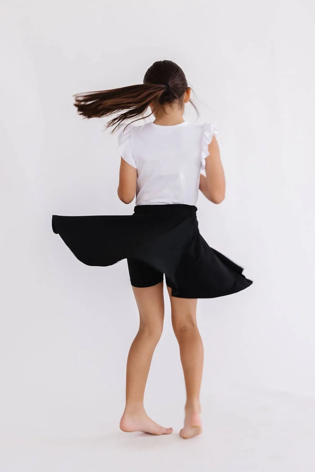 girl wearing black twirl skort for girls spinning with hair flying and white ruffle sleeve shirt