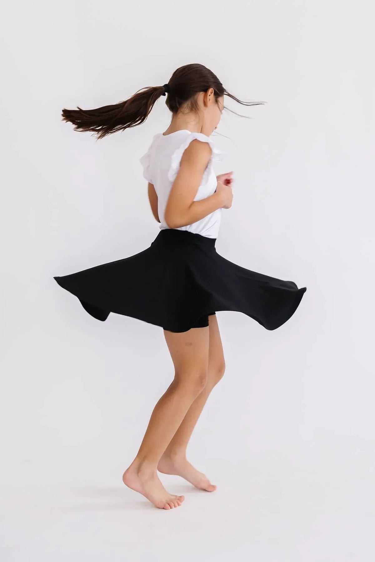 young girl twirling in black twirl skort for girls by Mila & Rose in a white sleeveless top