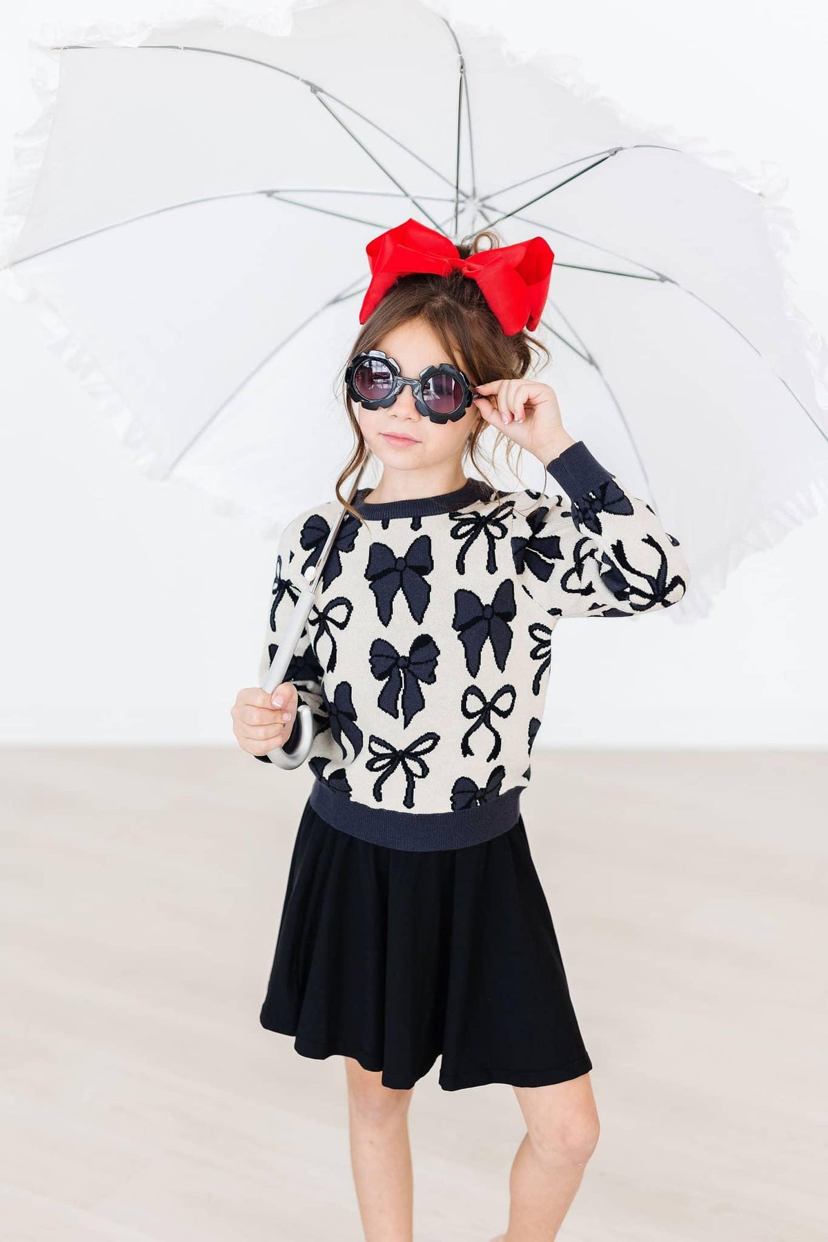 girl wearing black twirl skort for girls holding a white umbrella and wearing a red bow