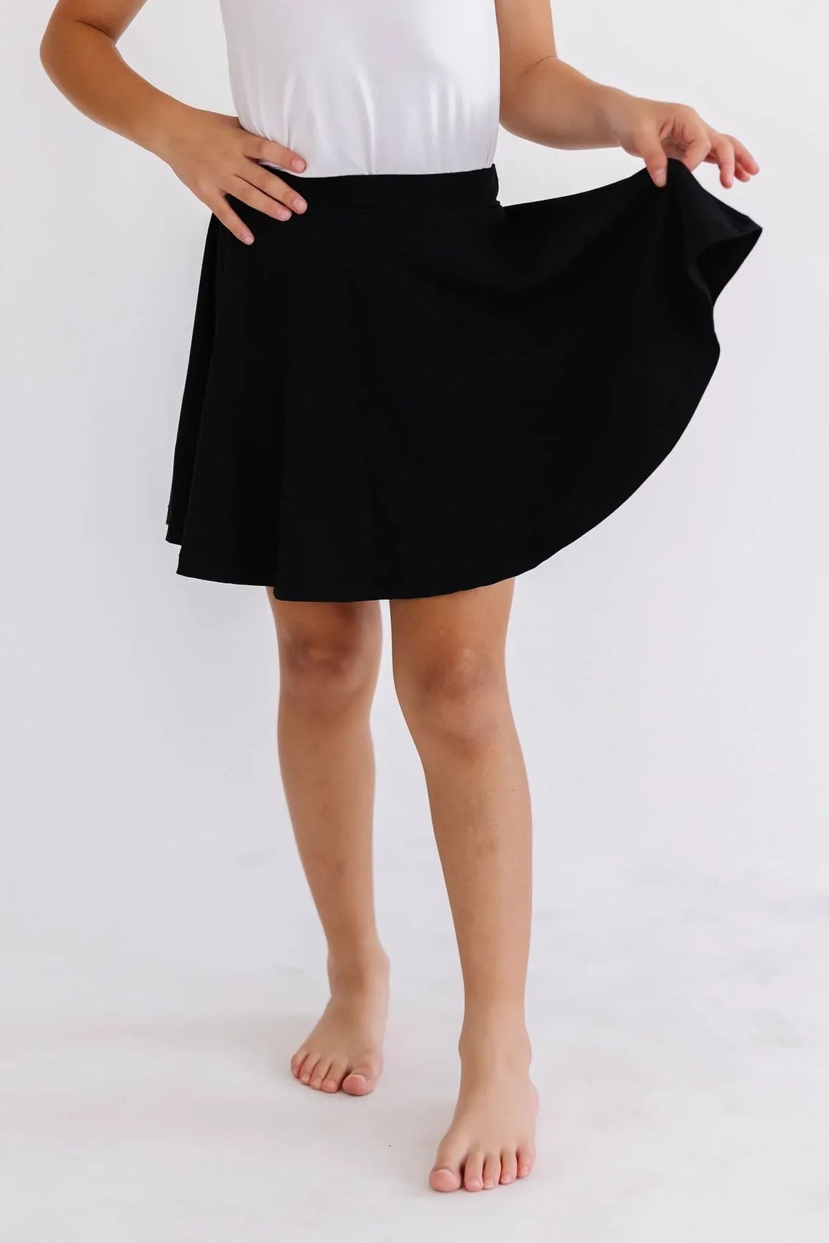girl wearing black twirl skort for girls holding the skirt while standing barefoot