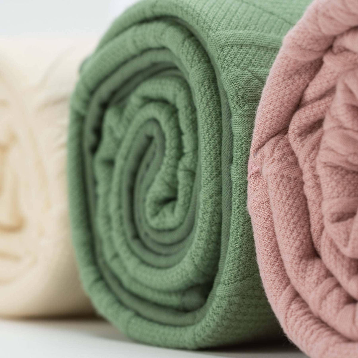 Rolled knit baby blankets in green, pink, and cream, perfect for newborns