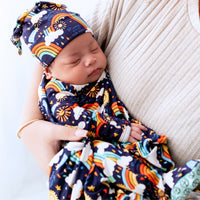 Newborn wearing The SoftKnot Cap Here Comes the Sunshine Blue, a bamboo hat with sun and rainbow print.