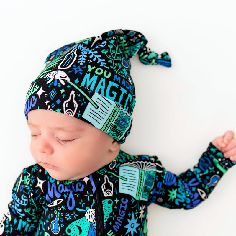 Newborn wearing The SoftKnot Cap by Mystic Mama Blue featuring a blue-green botanical print.