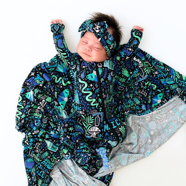 Baby wearing blue Mystic Mama second-skin footie with zip and matching printed headband.