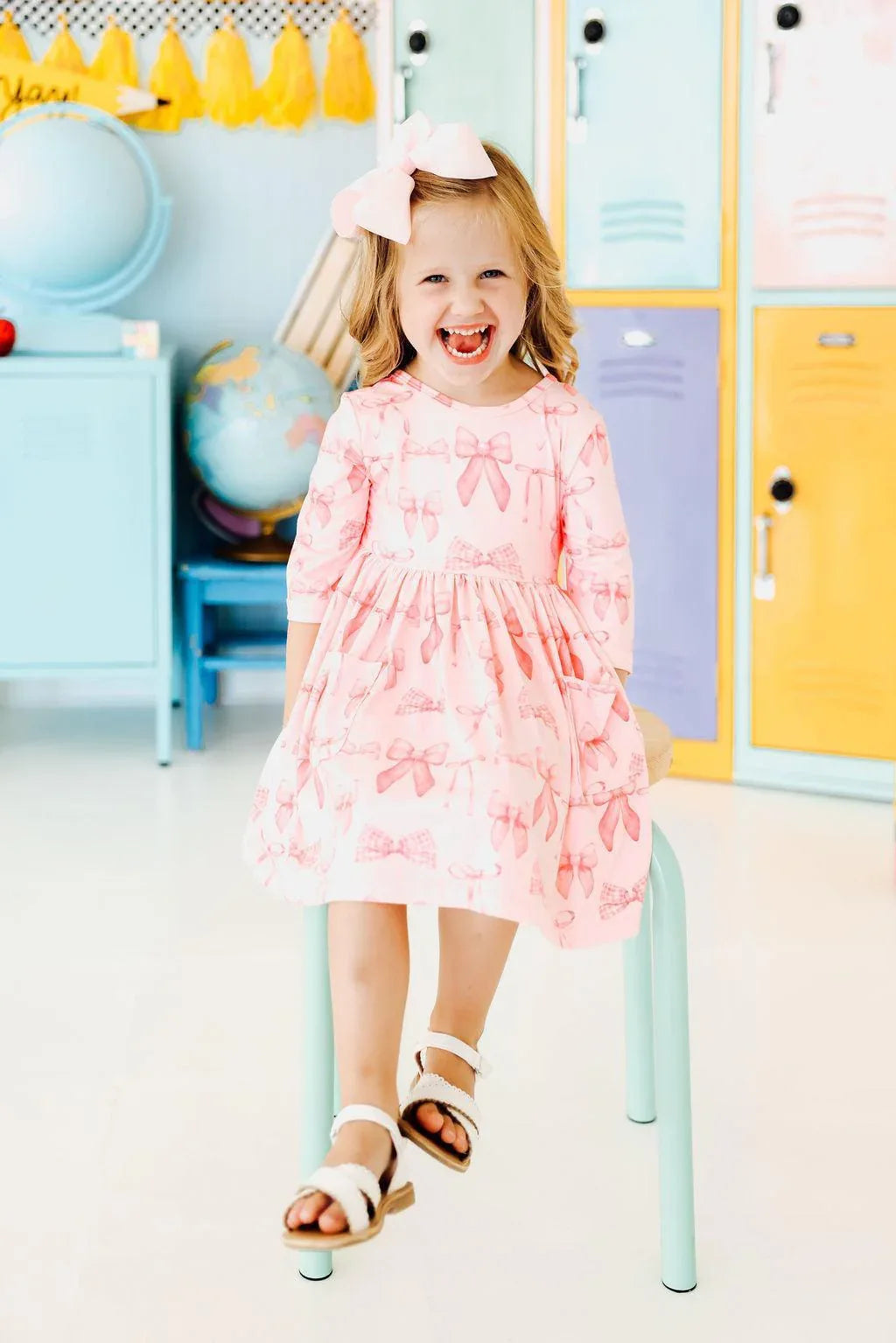 Young girl wearing pink blushing bows twirly dress for girls sitting on a chair smiling