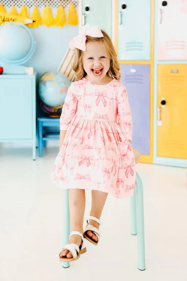 Young girl wearing pink blushing bows twirly dress for girls sitting on a chair smiling