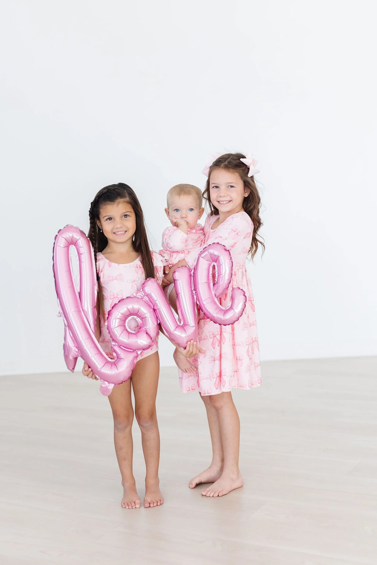 Two girls in pink blushing bows twirly dress for girls holding love balloon and baby in matching outfit