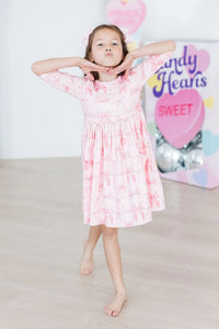 Young girl wearing a pink blushing bows twirly dress for girls posing with hands under chin barefoot