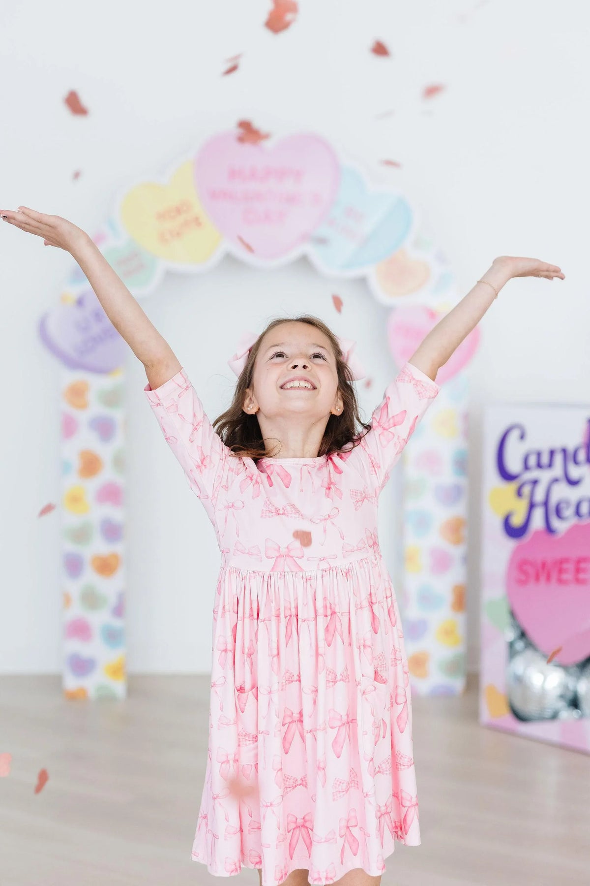 Young girl wearing a pink blushing bows twirly dress for girls with 3/4 sleeves raising her arms joyfully