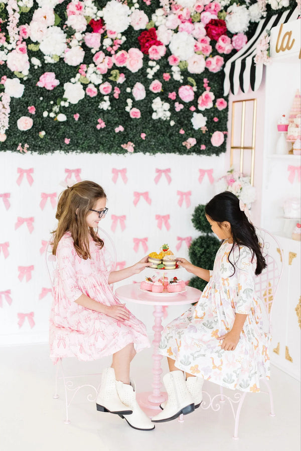 Two girls sitting and enjoying tea party wearing blushing bows twirly dress for girls in pink and floral prints
