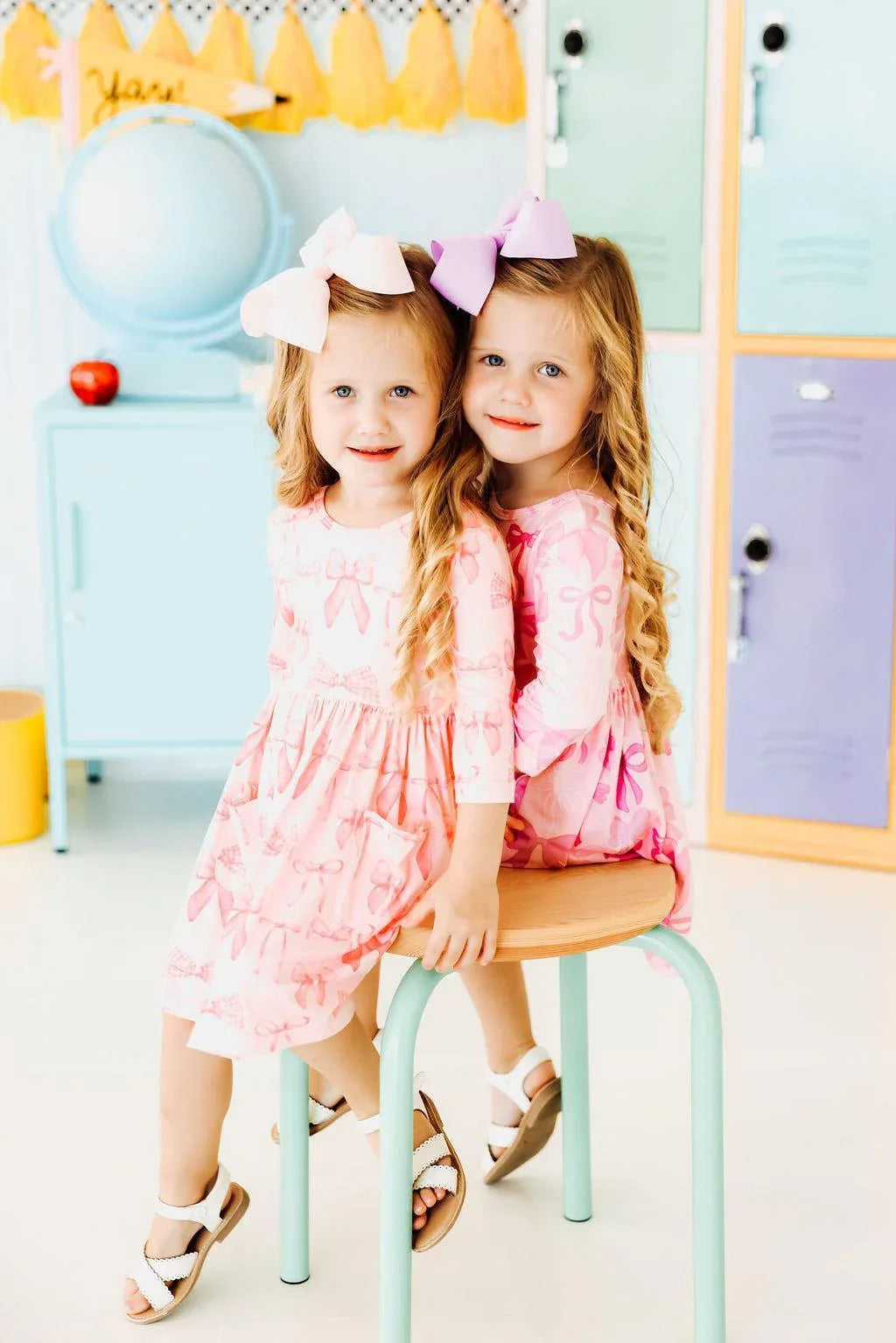 Two young girls wearing pink blushing bows twirly dress for girls sitting and smiling indoors