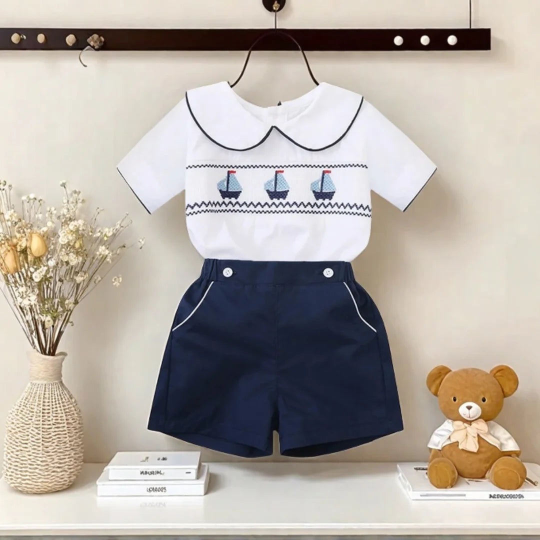 White cotton boys smocked sailboat outfit with navy blue shorts and smocked sailboat detail