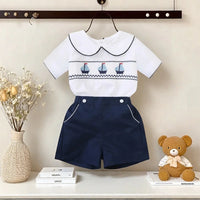 White cotton boys smocked sailboat outfit with navy blue shorts and smocked sailboat detail