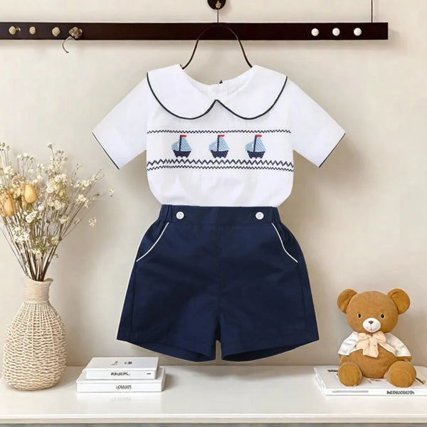 White cotton boys smocked sailboat outfit with navy blue shorts and smocked sailboat detail