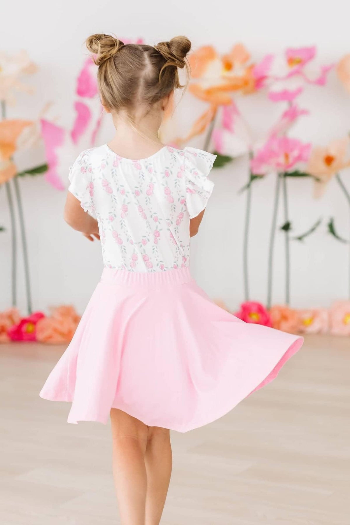 Young girl wearing bubblegum pink twirl skort for girls spinning indoors with floral background