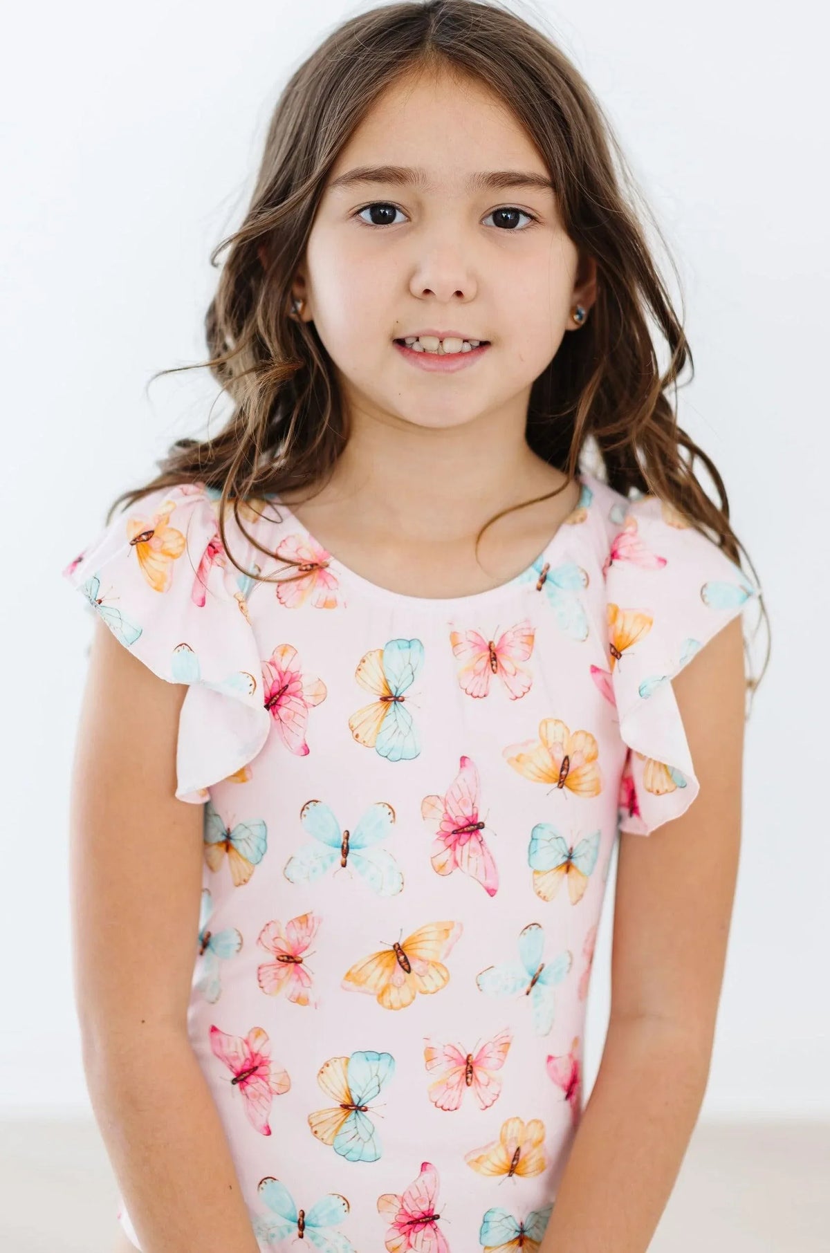Girl wearing pink butterfly flutter sleeve baby leotard with colorful butterfly print standing and smiling