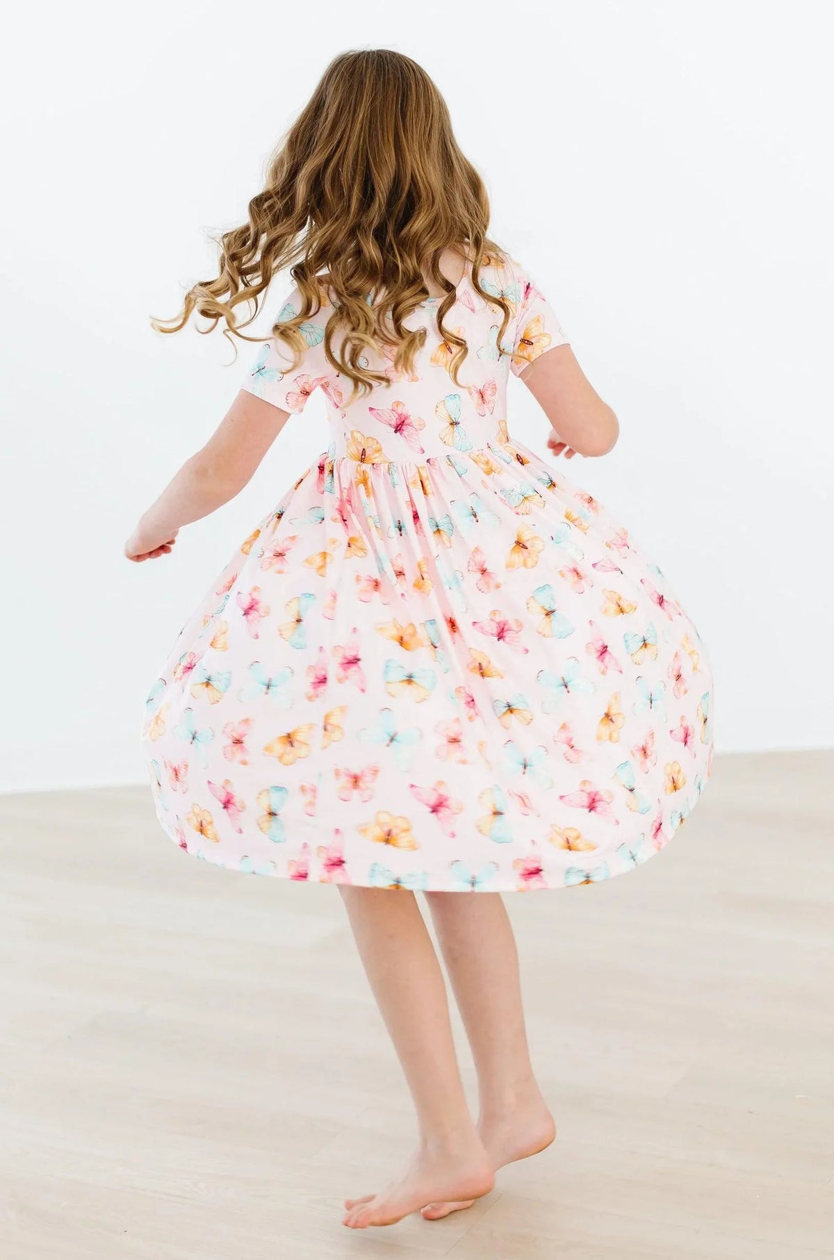 Girl twirling in a white butterfly print twirl dress for girls with short sleeves and colorful butterfly patterns