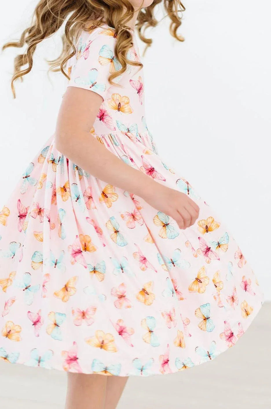 Girl wearing white butterfly print twirl dress for girls with pink and blue butterflies spinning