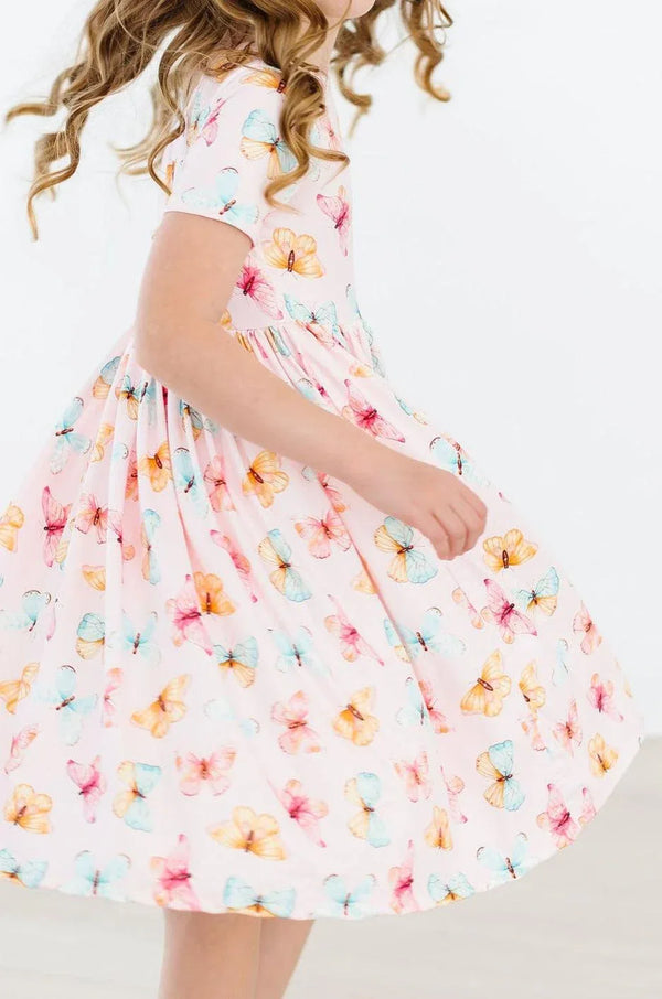 Girl wearing white butterfly print twirl dress for girls with pink and blue butterflies spinning