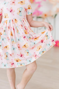 young girl wearing butterfly print twirl dress for girls in pastel pink holding skirt out