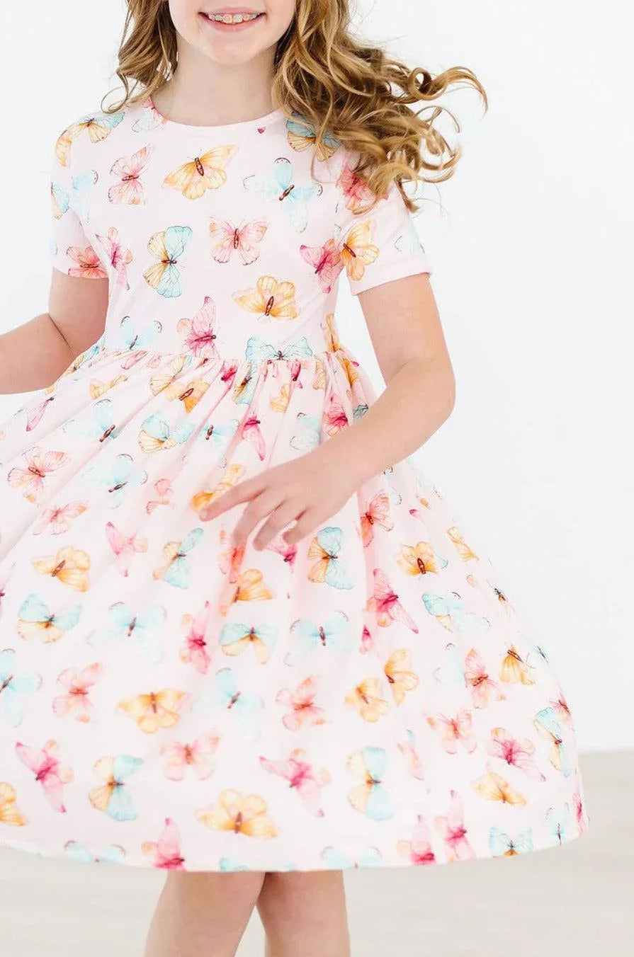 Girl wearing white butterfly print twirl dress for girls by Mila & Rose spinning with smile